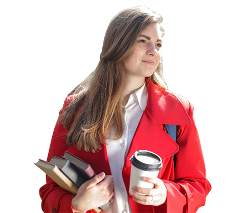 A student is smiling while holding a book and a coffee