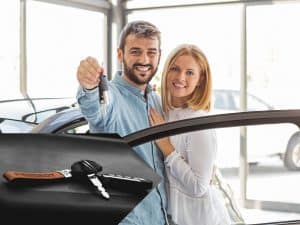 excited couple receiving keys to their new car and a close-up of car keys resting on black surface.