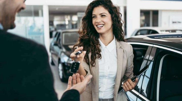 woman receiving car keys at auto dealership showroom